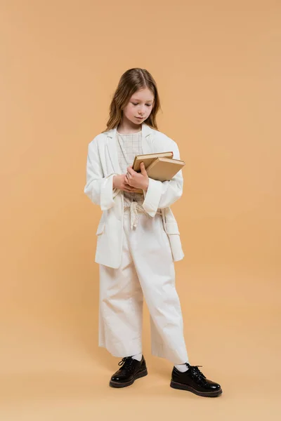 Education concept, preteen girl in white suit holding books and standing on beige background, fashionable outfit, formal attire, back to school, preparing for school new year — Stock Photo