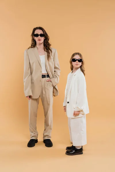Moderne Familie, Mutter und Tochter mit Sonnenbrille, stilvolle Geschäftsfrau und Mädchen in Anzügen posieren zusammen auf beigem Hintergrund, modische Outfits, formelle Kleidung, Corporate Mom — Stockfoto