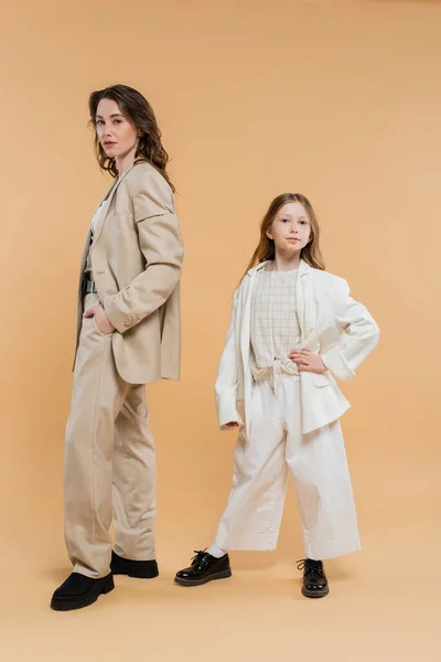 Stylish mother child concept, woman in suit and preteen daughter standing in suits on beige background, corporate mom, businesswoman, posing together, hand on hip, business style — Stock Photo