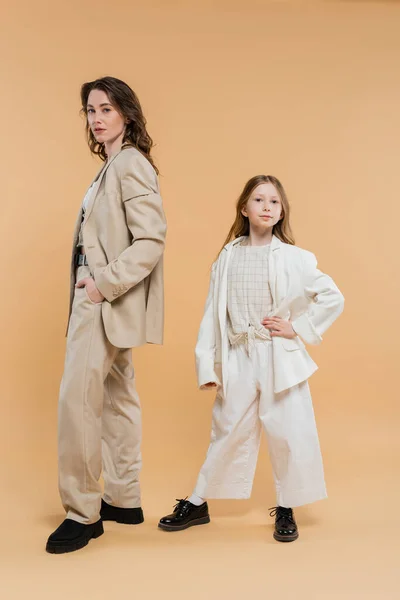 Concept élégant de mère enfant, femme en costume et fille préadolescente debout en costumes sur fond beige, mère d'entreprise, femme d'affaires, posant ensemble, main sur la hanche, style d'affaires — Photo de stock