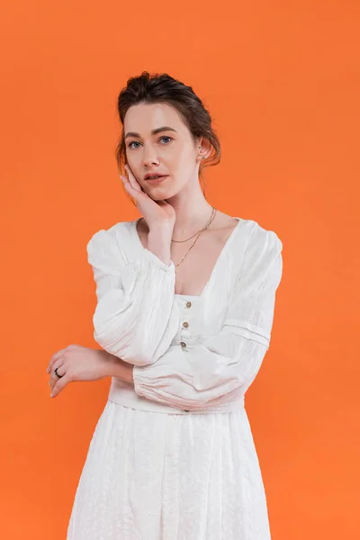 Літні тенденції, молода жінка в білому сонячному платті дивиться на камеру і стоїть на помаранчевому фоні, яскравий фон, стильна позування, леді в білому, модель моди, елегантність — стокове фото