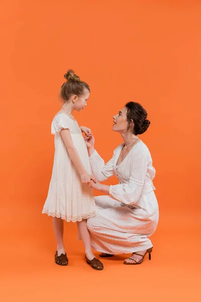 Tendências de verão, surpreendido jovem mãe de mãos dadas com a filha pré-adolescente no fundo laranja, vestidos de sol brancos, união, conceito de moda e estilo, ligação e amor — Fotografia de Stock