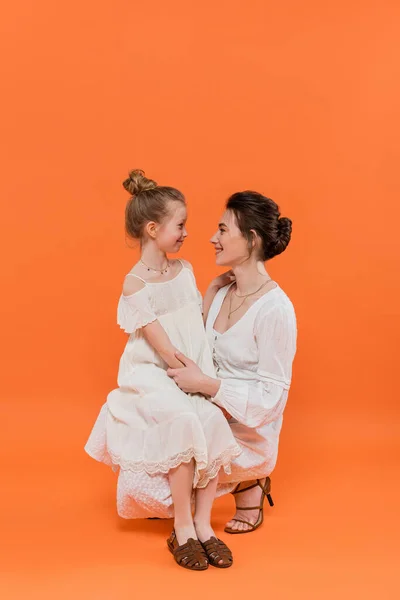 Summer trends, cheerful mother bonding with preteen daughter on orange background, white sun dresses, togetherness, fashion and style concept, motherly love, family bonding — Stock Photo