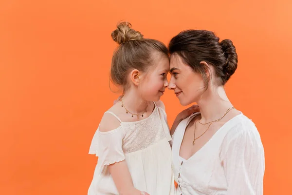 Sommertrends, Mutter-Tochter-Bindung, junge Frau und Frühchen posieren auf orangefarbenem Hintergrund, weiße Sonnenkleider, Zweisamkeit, Mode- und Stilkonzept, Nase an Nase — Stockfoto