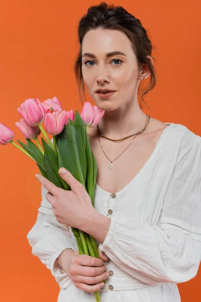 Bouquet of flowers, everyday fashion, young woman in white sun dress holding tulips and standing on orange background, lady in white, vibrant background, fashion and nature, summer — Stock Photo