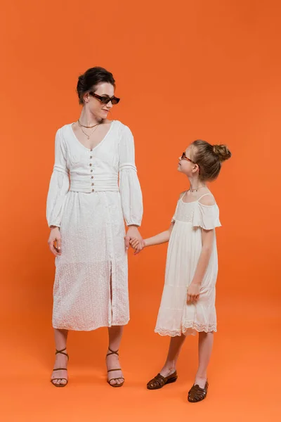 Mutterliebe, stilvolle Familie, Mutter und Kind in Sonnenbrille, Händchen haltend auf orangefarbenem Hintergrund, weiße Sonnenkleider weibliche Bindung, modisch, sommerlicher Stil, Glück — Stockfoto