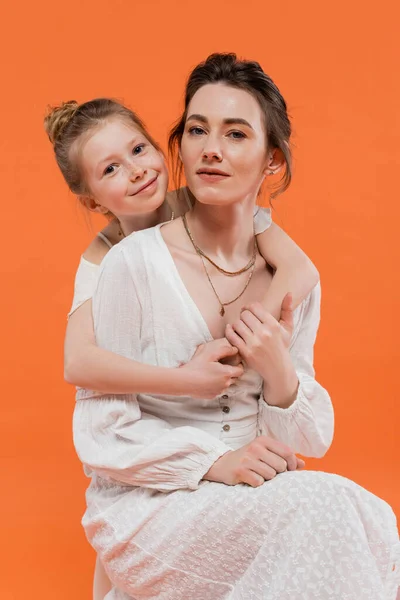 Mother and daughter, happy preteen girl hugging young woman on orange background, white sun dresses, modern parenting, summer fashion, togetherness, love, fashionable family — Stock Photo
