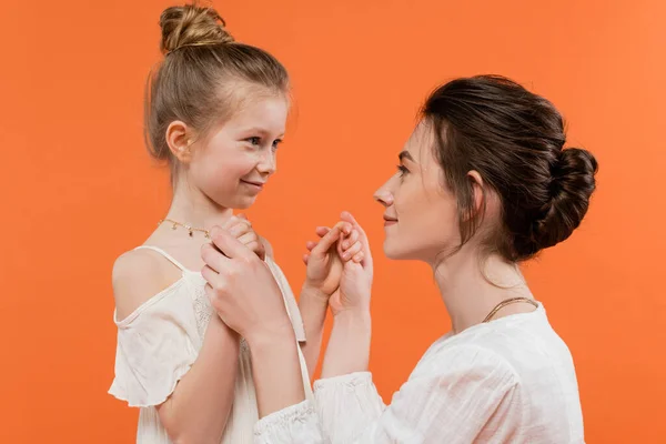 Mutterliebe, fürsorgliche Frau Händchenhalten mit ihrer Tochter auf orangefarbenem Hintergrund, moderne Elternschaft, Sommermode, weiße Sonnenkleider, Zweisamkeit, Liebe, weibliche Bindung — Stockfoto