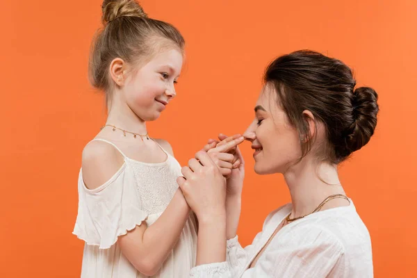 Family moment, happy preteen girl touching nose of mother on orange background, white sun dresses, modern parenting, summer fashion, togetherness, love, female bonding — Stock Photo