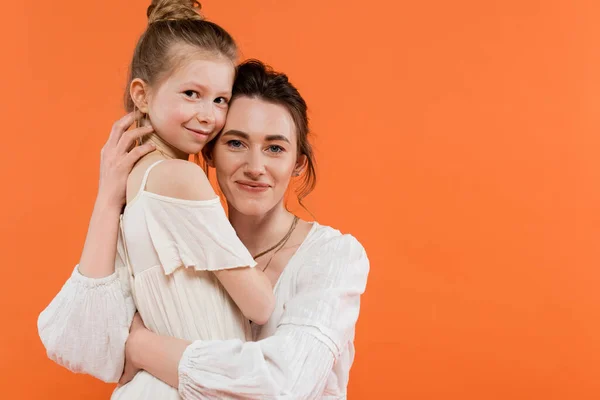 Сімейний зв'язок, радісна мати і дочка обіймають один одного на помаранчевому фоні посмішка, білі сонцезахисні сукні, сучасне батьківство, літня мода, взаємопочуття, мама і її дитина — стокове фото