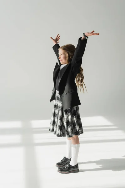 Estudante em uniforme, menina pré-adolescente alegre de pé com as mãos levantadas sobre fundo cinza, traje formal, criança na moda, alegre, emoção, celebração da aprendizagem, de volta ao conceito da escola — Fotografia de Stock