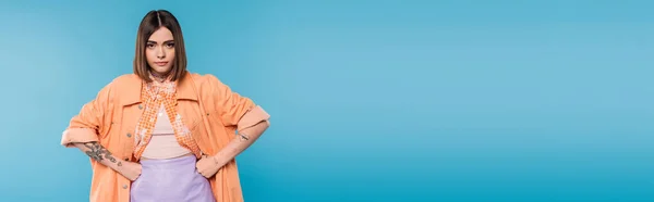Offended woman standing with hands on hips on blue background, looking at camera, emotional, displeased, generation z, short brunette hair, pierced nose, tattooed, banner — Stock Photo