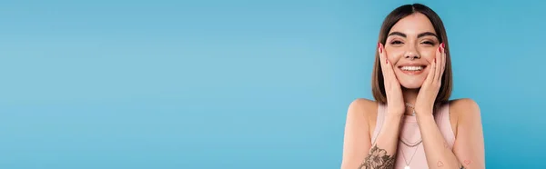 Positivity, tattooed young woman with short hair in tank top smiling and touching her face on blue background, casual attire, gen z fashion, happiness, joyful face, banner — Stock Photo