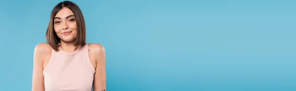Not knowing, positive young woman with tattoos and nose piercing standing in tank top on blue background, looking at camera, confused, pretty face, generation z, summer outfit, banner — Stock Photo