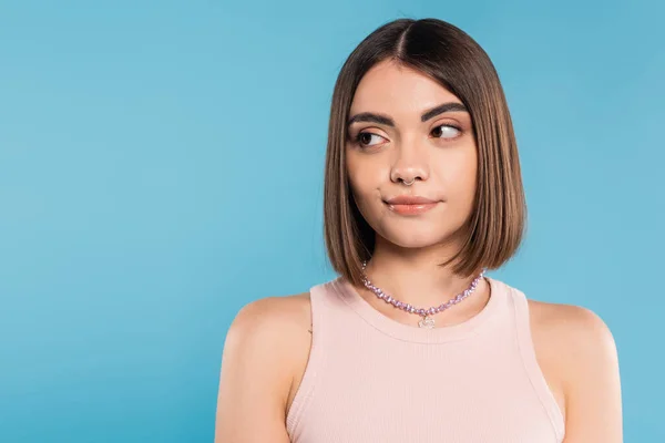 Doubting, young brunette woman with short hair and nose piercing standing in tank top and looking away on blue background, youth culture, skepticism, generation z, summer fashion — Stock Photo