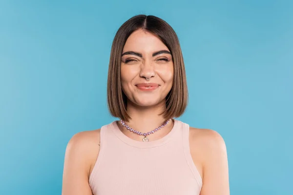 Positivity, cheerful young woman with short hair, nose piercing and tank top smiling on blue background, generation z, fashionable, personal style, silver necklace, emotional, happiness — Stock Photo