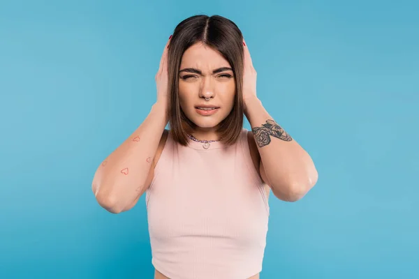 Migraine, tattooed young woman with nose piercing and short hair touching head while suffering from headache on blue background, generation z, tiredness, stress — Stock Photo