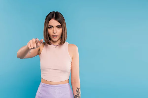 Pointing at camera, emotional young woman with short hair, tattoos and pose piercing gesturing on blue background, generation z, displeased, casual attire, everyday makeup — Stock Photo