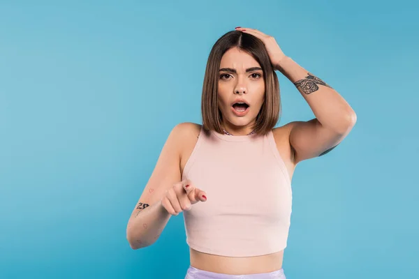 Shocked face, brunette young woman with short hair, tattoos and nose piercing pointing at camera on blue background, generation z, displeased, casual attire, summer outfit — Stock Photo