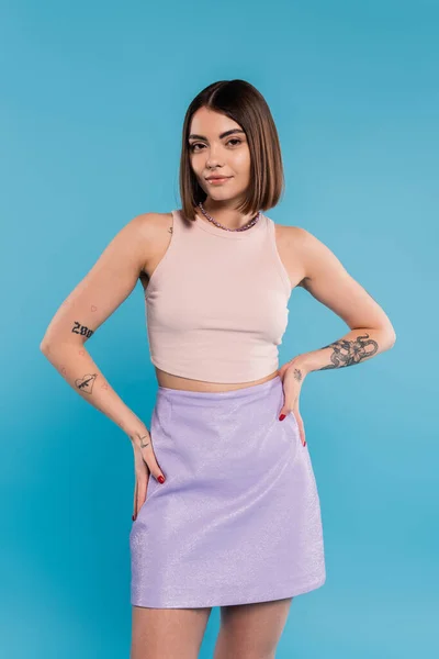Summer outfit, casual attire, happy young woman with short hair, tattoos and nose piercing standing with hands on hips on blue background, generation z, everyday style — Stock Photo