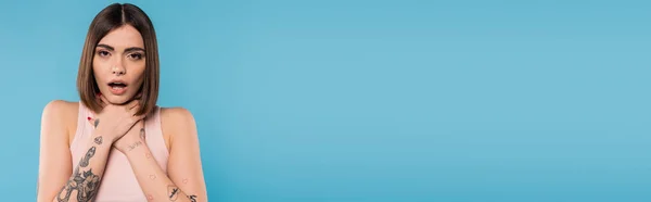 Brunetta giovane donna con i capelli corti si tiene per mano vicino al collo e in piedi con la bocca aperta mentre soffocava sullo sfondo blu, abbigliamento casual, gen z moda, stile personale, piercing al naso, banner — Foto stock