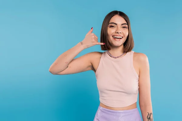 Showing call me, happy young woman with short hair gesturing and looking at camera on blue background, casual attire, gen z fashion, personal style, nose piercing, positivity — Stock Photo