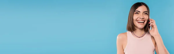 Telefonanruf, Positivität, glückliche junge Frau mit kurzen Haaren, Tätowierungen und Nasenpiercing, die auf dem Smartphone auf blauem Hintergrund spricht, lässige Kleidung, Gen-Z-Mode, persönlicher Stil, Banner — Stockfoto