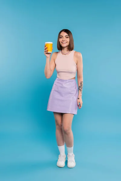 Coffee to go, cheerful young woman with short hair, tattoos and nose piercing holding paper cup on blue background, generation z, summer trends, attractive, coffee culture — Stock Photo