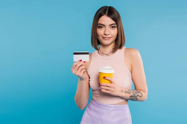 To go coffee, happy young woman with short hair, tattoos and nose piercing holding paper cup and credit card on blue background, generation z, summer trends, attractive, coffee culture — Stock Photo