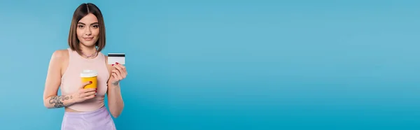 Coffee to go, fröhliche junge Frau mit kurzen Haaren, Tätowierungen und Nasenpiercing, Pappbecher und Kreditkarte auf blauem Hintergrund, Generation Z, Sommertrends, attraktiv, Kaffeekultur, Banner — Stockfoto