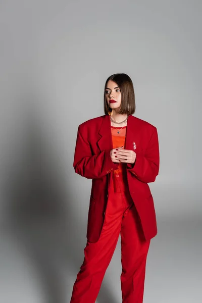 Dame in Rot, junge brünette Frau mit kurzen Haaren und Nasenpiercing posiert im Anzug auf grauem Hintergrund, Generation Z, Führungsstil, modisches Modell, professionelle Kleidung, Führungsstil — Stockfoto