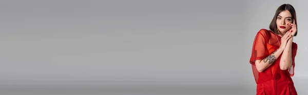 Modella fashion, abito rosso, giovane donna tatuata con capelli corti e piercing al naso posa in camicetta rossa trasparente su sfondo grigio, stile moderno, generazione z, tendenza moda, banner — Foto stock