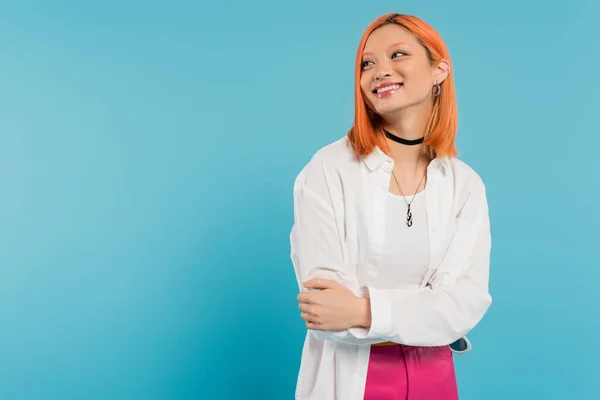 Glücklich, fröhliche asiatische junge Frau mit gefärbten Haaren, lässig gekleidet und lächelnd auf blauem Hintergrund, weißes Hemd, wegguckend, Halskette, rote Haare, Generation z — Stockfoto