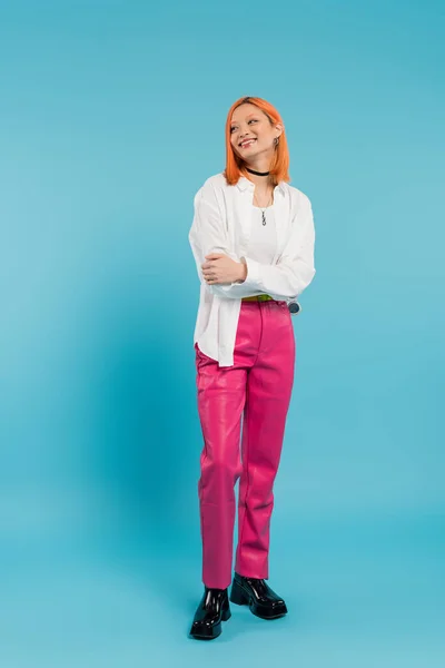 Happy face, cheerful asian young woman with dyed hair standing in casual attire and smiling on blue background, white shirt, looking away, choker necklace, red hair, generation z, full length — Stock Photo