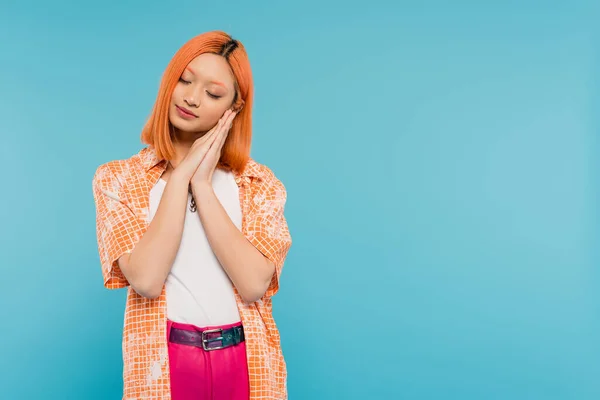 Sleepy asian woman, young model with dyed red hair holding hands near face and posing with closed eyes on vibrant blue background, generation z, casual attire, tired, fatigue, exhausted — Stock Photo