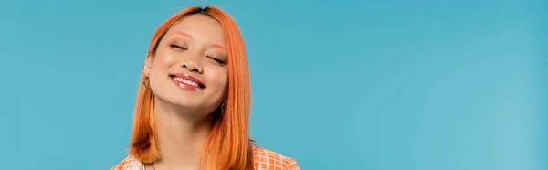 Visage heureux, sourire radieux, jeune femme asiatique aux cheveux teints debout avec les yeux fermés en chemise orange et souriant sur fond bleu, tenue décontractée, bonheur, liberté, attitude gaie, bannière — Photo de stock