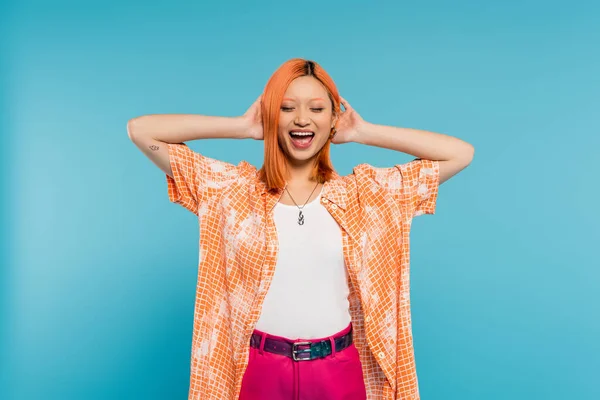 Positividade e felicidade, jovem mulher asiática com cabelo tingido em pé com olhos fechados em camisa laranja e sorrindo no fundo azul, traje casual, liberdade, atitude alegre, tatuagem — Fotografia de Stock
