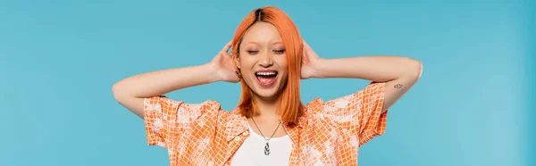 Positivité et bonheur, jeune femme asiatique aux cheveux teints debout les yeux fermés en chemise orange et souriant sur fond bleu, tenue décontractée, liberté, attitude gaie, tatouage, bannière — Photo de stock