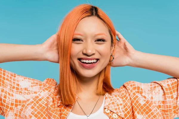 Positividad, sonrisa radiante, joven mujer asiática con el pelo teñido de pie en camisa naranja y sonriendo sobre fondo azul, atuendo casual, libertad, actitud alegre, mirando a la cámara - foto de stock