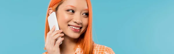 Positivität, Mobilkommunikation, fröhliche und junge asiatische Frau, die auf Smartphone spricht und auf blauem Hintergrund wegsieht, lässiger Stil, modisch, Gespräch, Telefonat, Banner — Stockfoto