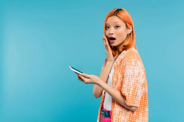Überraschtes Gesicht, Social Media Influencer, junge asiatische Frau mit gefärbten Haaren mit Smartphone auf blauem Hintergrund, Mobiltelefon, Jugendkultur, digitales Zeitalter, Messaging, Generation z — Stockfoto