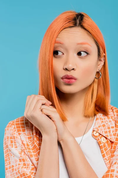 Retrato, jovem mulher asiática curiosa com cabelo curto e tingido, maquiagem natural e brincos de argola olhando para o fundo azul, camisa laranja, geração z, lábios amuados, emoção — Fotografia de Stock