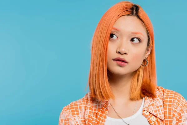 Portrait, thinking and looking away, pensive young asian woman with short and dyed hair, natural makeup and hoop earrings on blue background, orange shirt, generation z, biting lip — Stock Photo