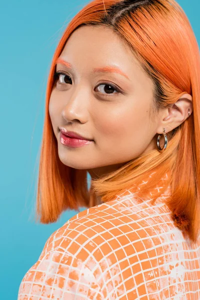 Portrait de jeune femme asiatique avec maquillage naturel, brillant à lèvres, boucles d'oreilles cerceau et cheveux teints courts regardant la caméra sur fond bleu, jeunesse, génération z, mode, tenue décontractée — Photo de stock