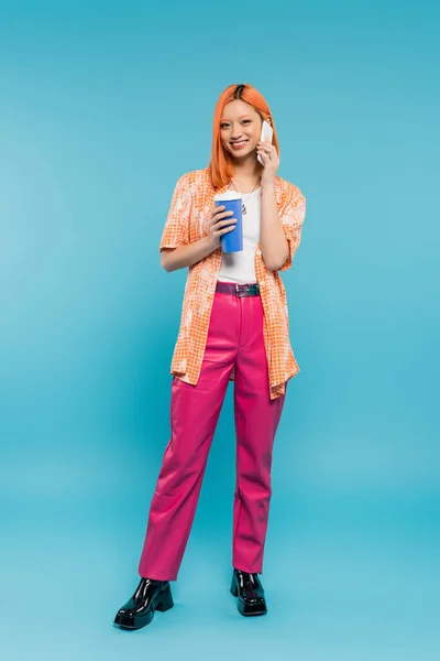 Full length, phone call, happy asian and young woman with red hair holding paper cup and talking on smartphone on blue background, casual attire, generation z, coffee culture, takeaway — Stock Photo