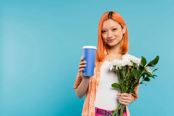 Позитивность, счастливая азиатская и молодая женщина с рыжими волосами проведение кофе в бумажной чашке и букет цветов на голубом фоне, случайный наряд, поколение z, культура кофе, горячий напиток — стоковое фото