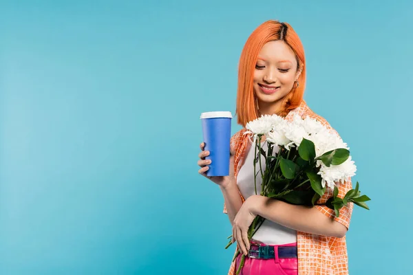 Vibes printanières, joyeuse asiatique et jeune femme aux cheveux roux tenant tasse en papier et bouquet de fleurs sur fond bleu, tenue décontractée, génération z, culture du café, boisson chaude, café à emporter — Photo de stock