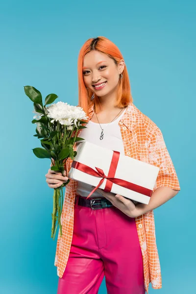 Floral bouquet, holiday, present, joyful and young asian woman with dyed hair holding white flowers and gift box on blue background, casual attire, generation z, festive celebration, birthday — Stock Photo