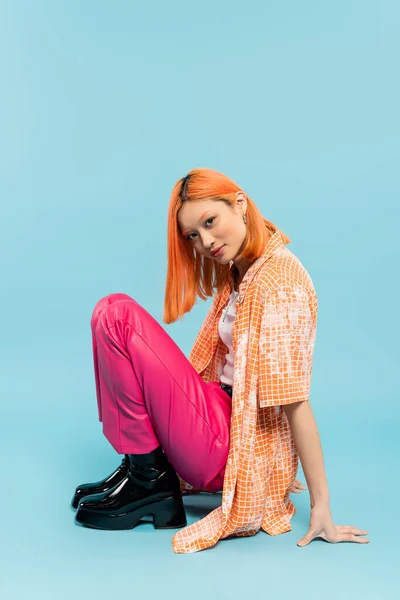 Pleased face, summer vibes, youthful and fashionable asian woman with colored red hair looking at camera on blue background, casual clothes, orange shirt, pink pants, generation z — Stock Photo