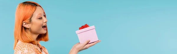 Pleasant surprise, excitement, delighted asian woman with dyed red hair and open mouth looking at gift box on blue background, happy summer, vibrant lifestyle, generation z, banner — Stock Photo